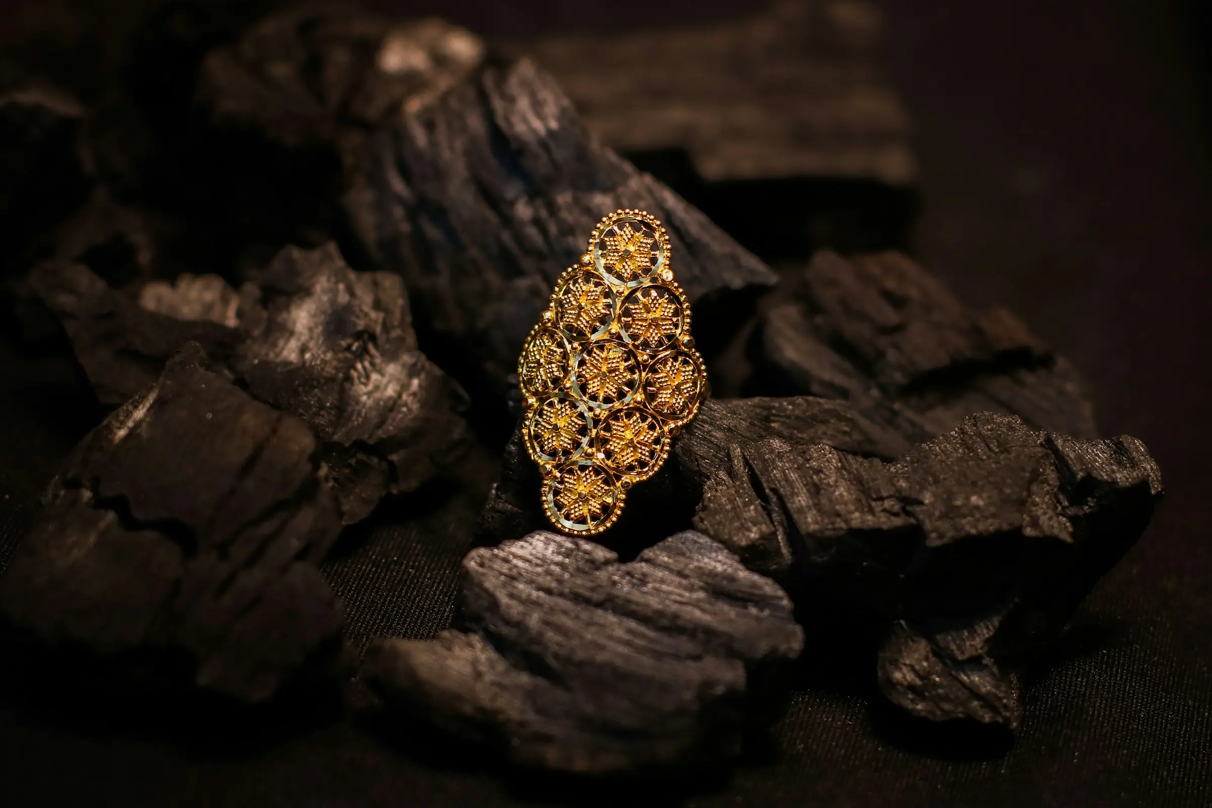 Un anello in filigrana d'oro appoggiato sul carbone